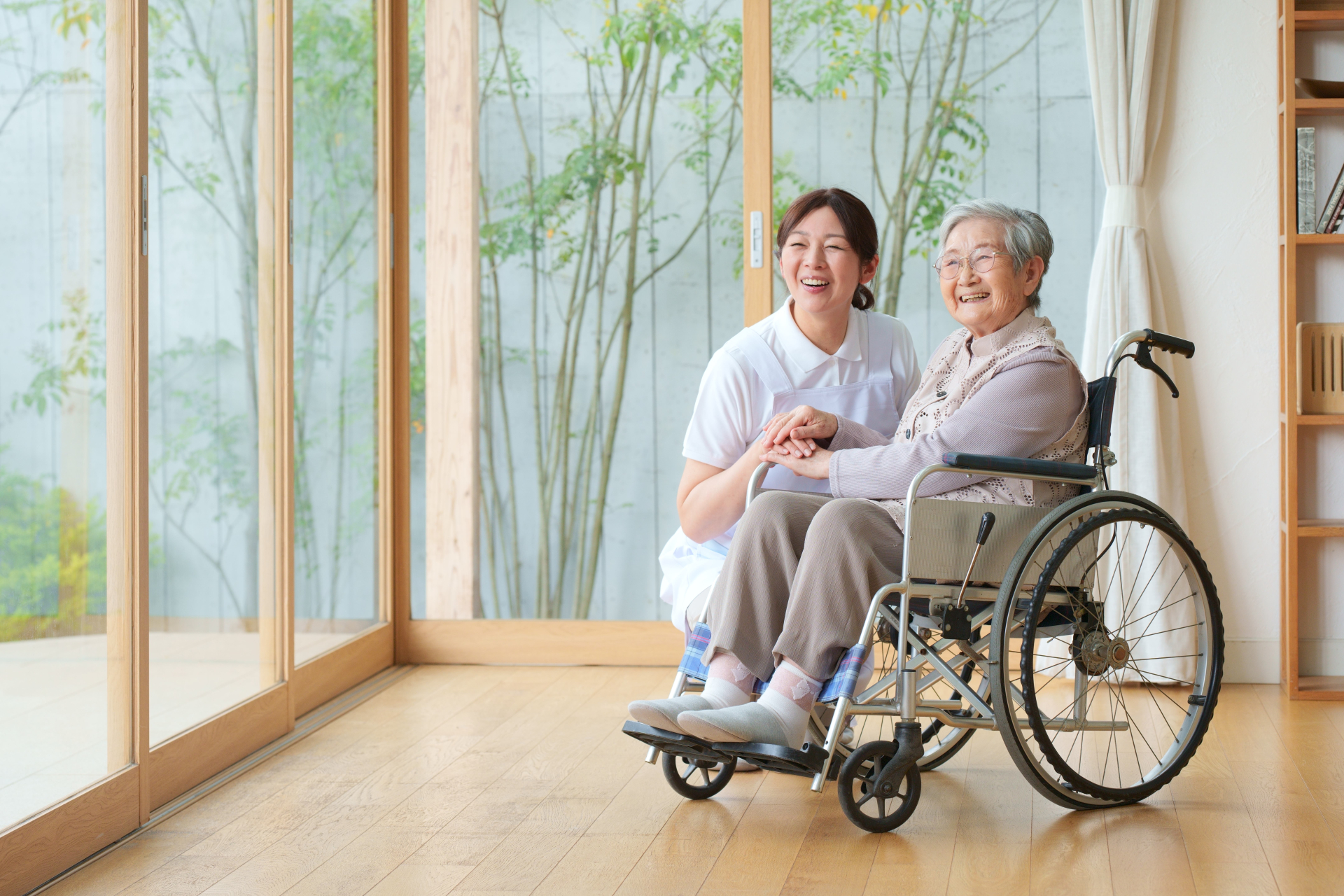 窓の外を眺める車椅子に乗った高齢女性と介護士