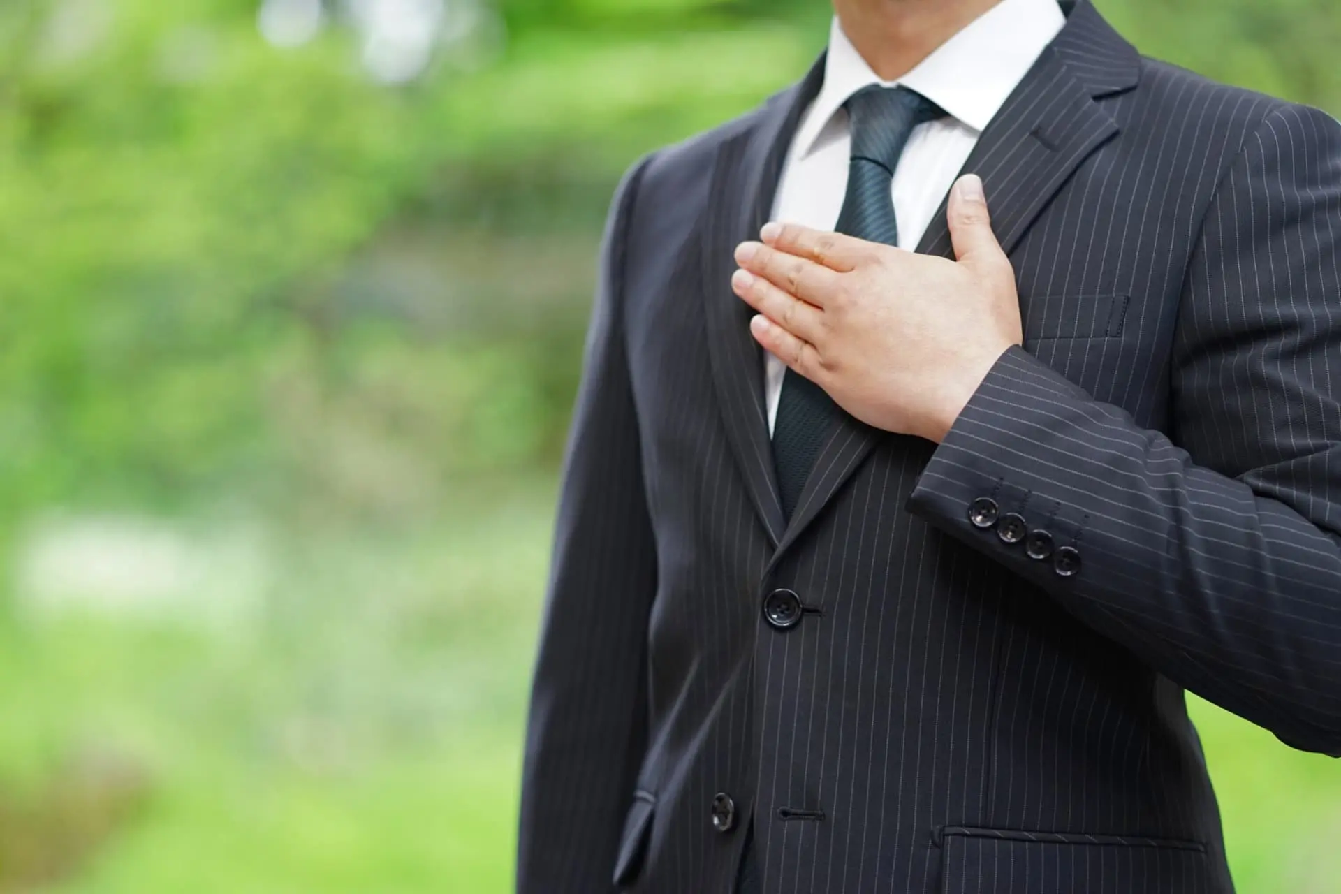 スーツ姿のビジネスマンが、胸に手を当てて屋外に立っている写真