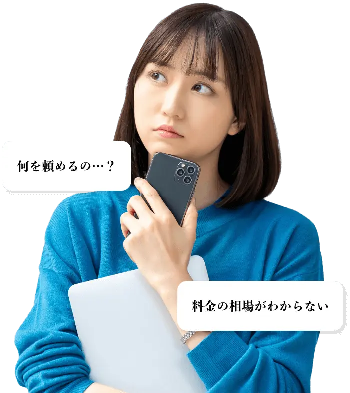 スマートフォンとパソコンを抱えて、サービスの詳細や料金について考えている、青いセーターを着た若い女性の写真