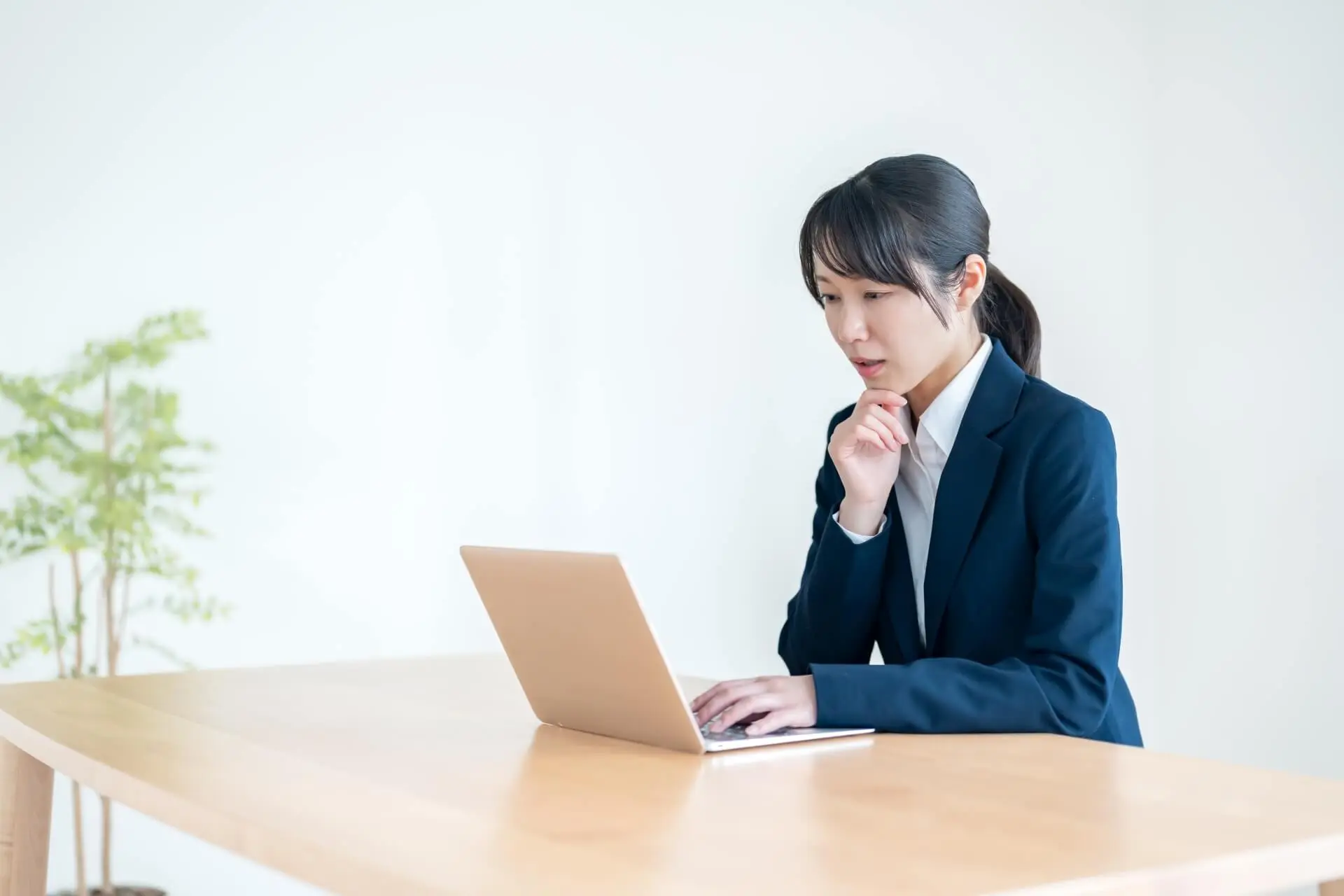 スーツ姿の女性が机でパソコンを操作している写真