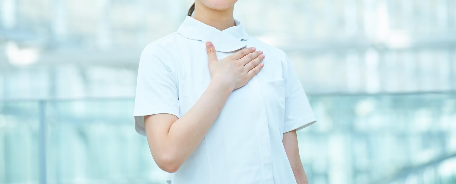 白衣姿の女性看護スタッフが胸に手を当てている様子の写真