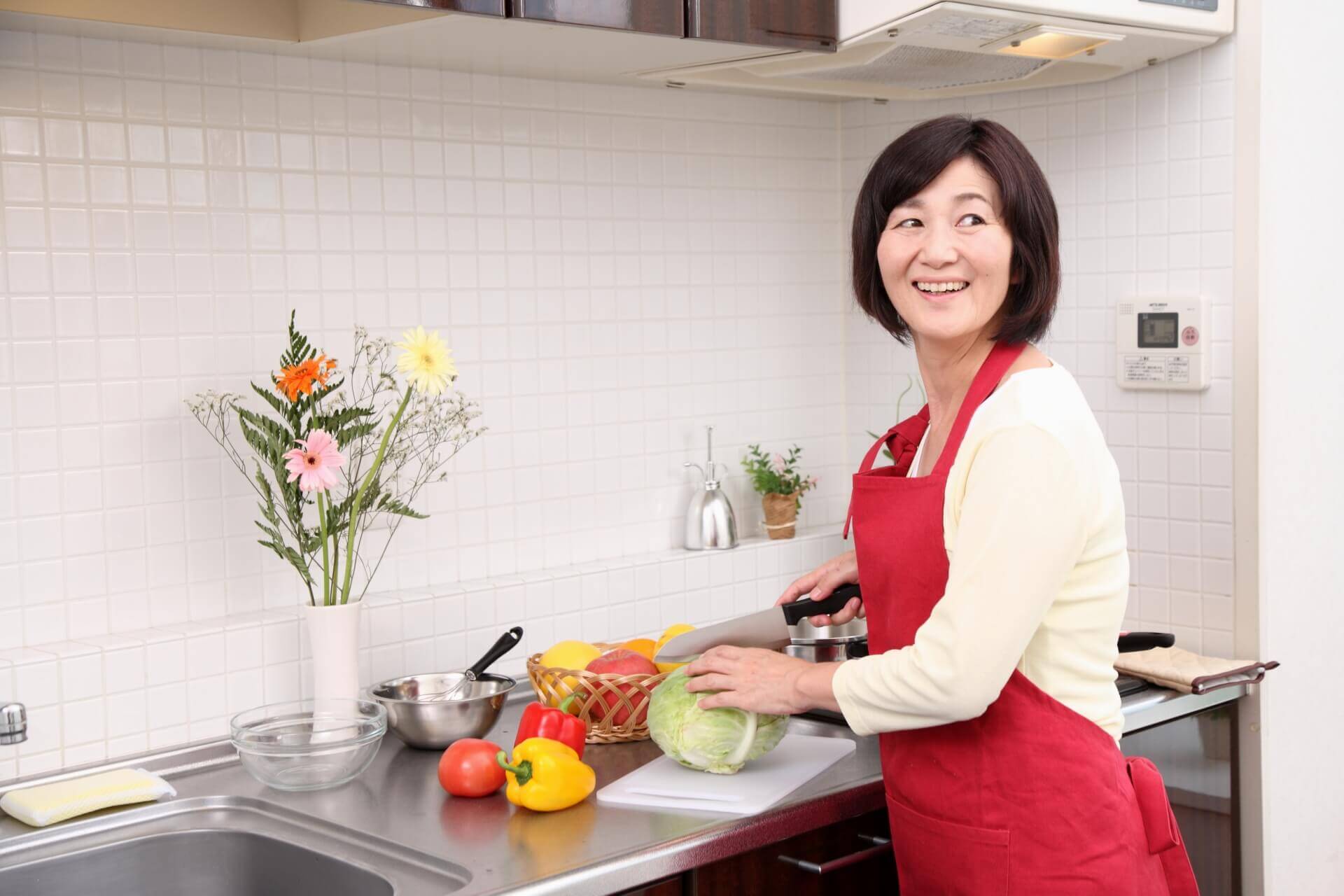 エプロンを身につけてキッチンで料理をしながら、笑顔で振り返る女性スタッフのイメージ写真