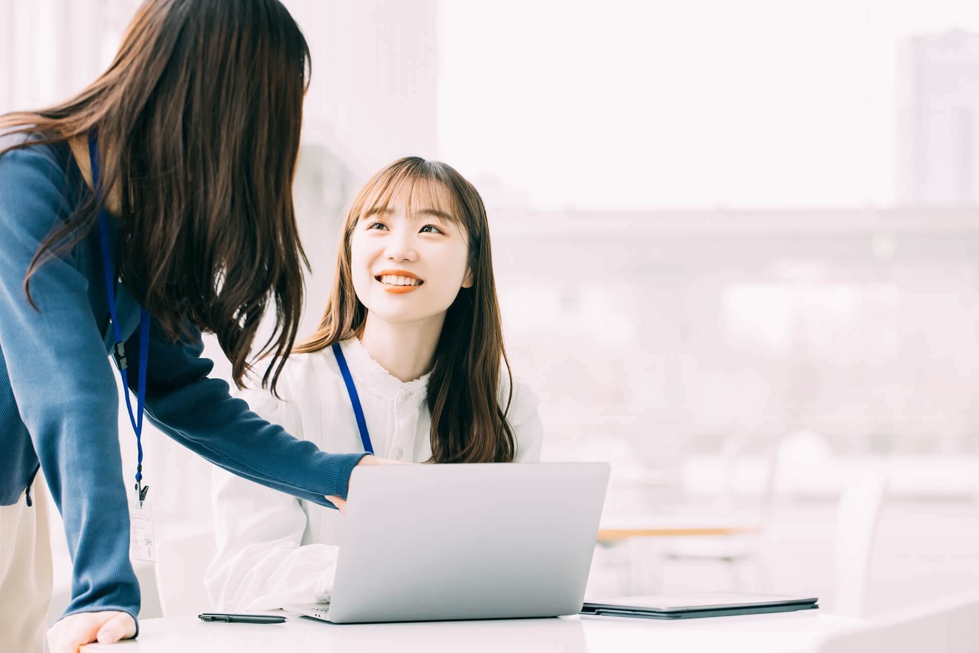 デスクで同僚と明るい笑顔で会話をする女性スタッフのイメージ写真