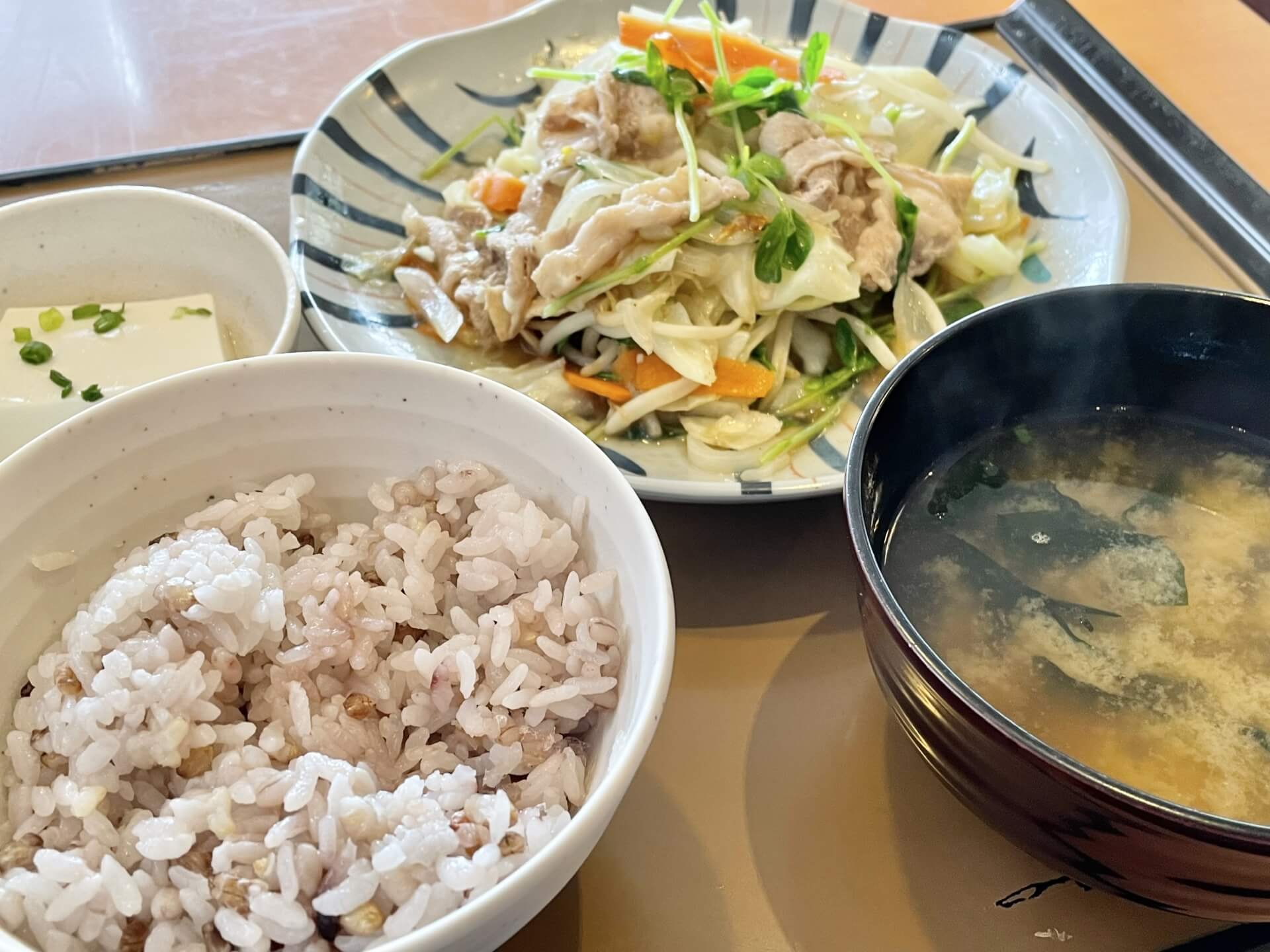 白米と味噌汁、豆腐、野菜炒めがトレイに載っている写真