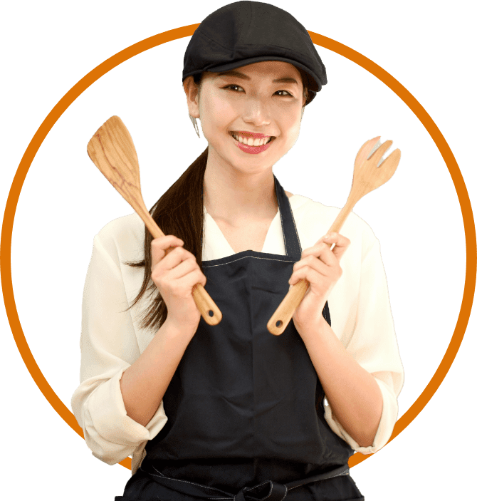 調理器具を持って、笑顔でこちらを見つめている、エプロン姿の女性料理代行スタッフの写真