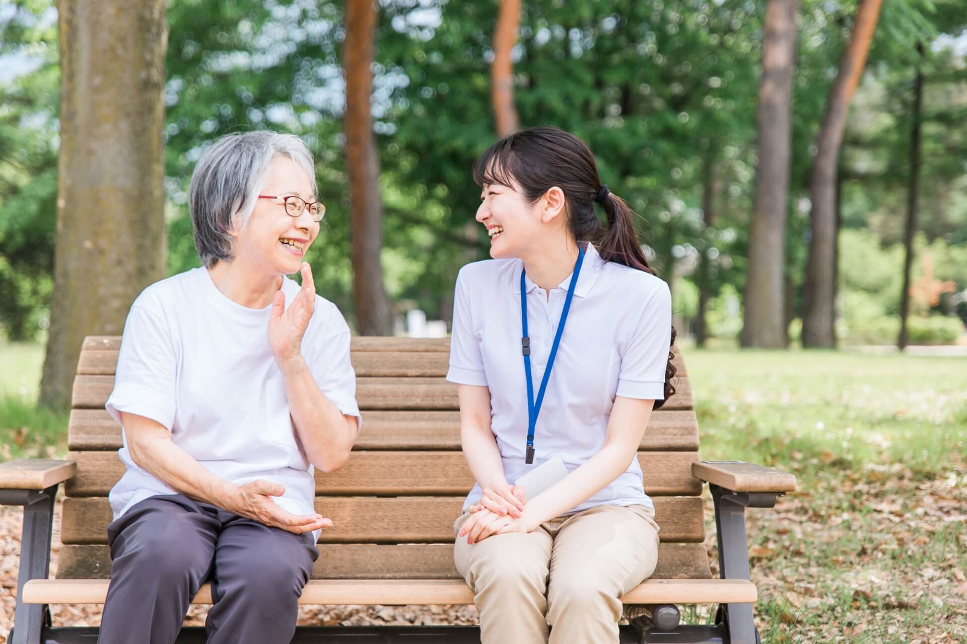 屋外のベンチに座り、親しく会話する高齢女性と介護スタッフの写真