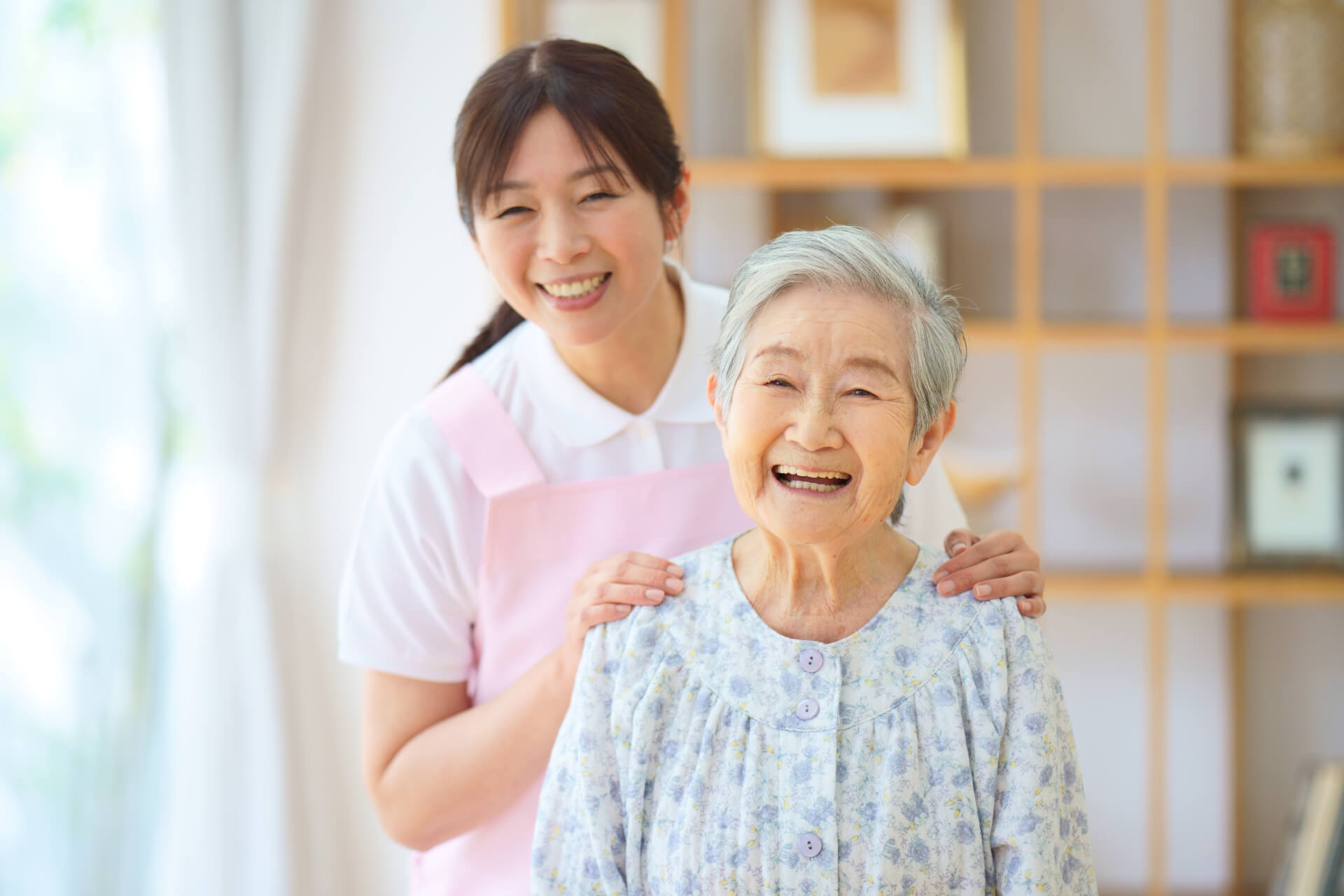 一緒に笑う女性介護スタッフと高齢者女性の写真