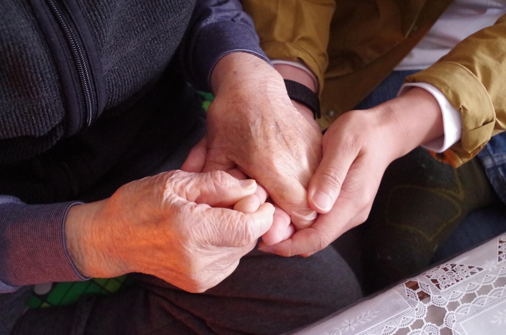 高齢者の手を両手で握る、介護スタッフの手元の写真