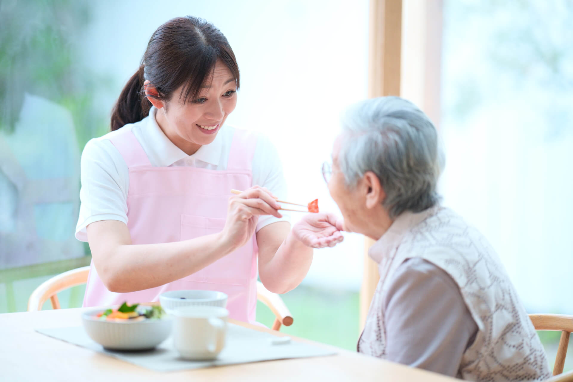 ご高齢女性の食事を手助けする介護/看護スタッフの写真