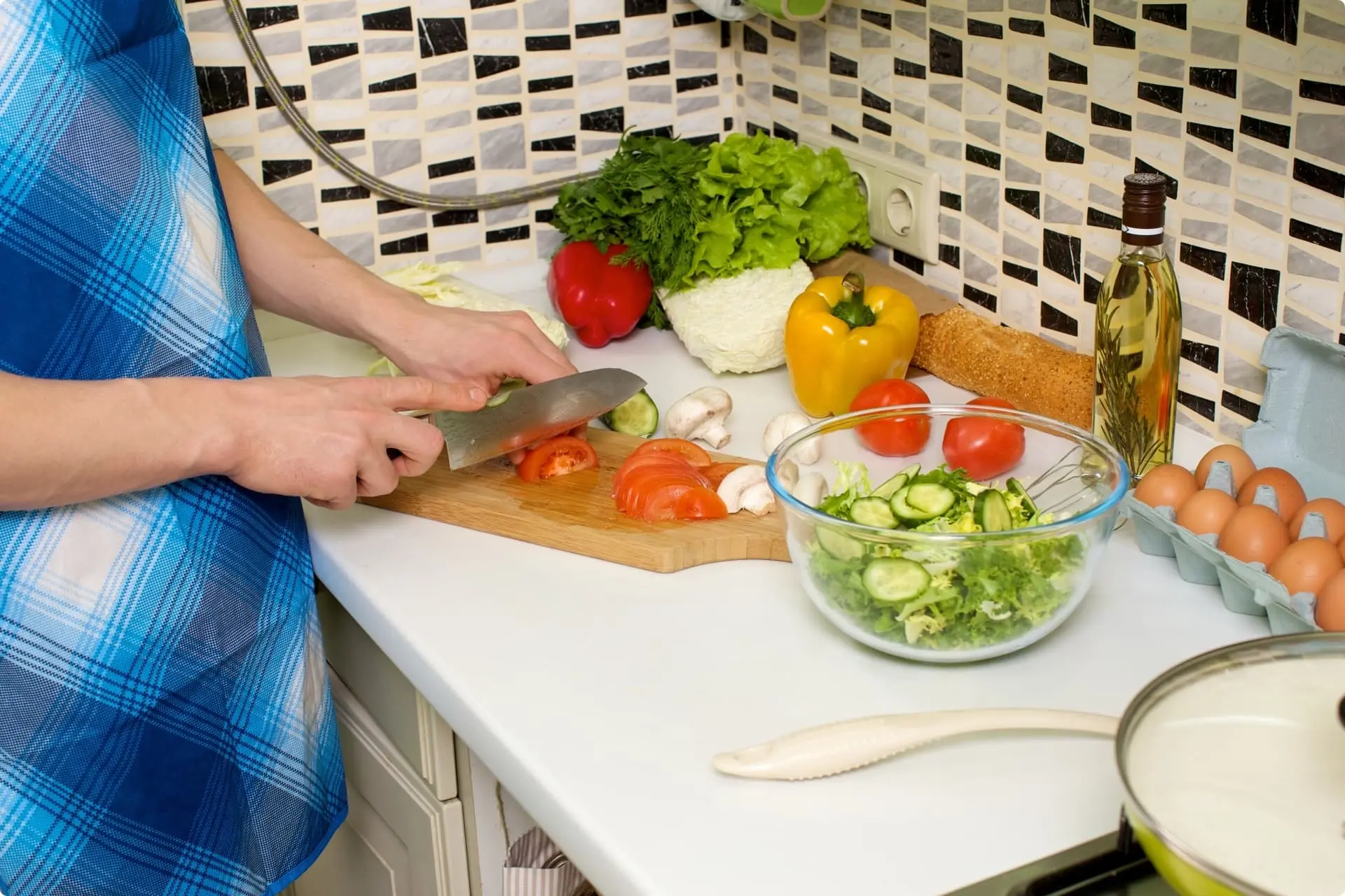 女性家事代行スタッフが台所で野菜を切り、調理している写真