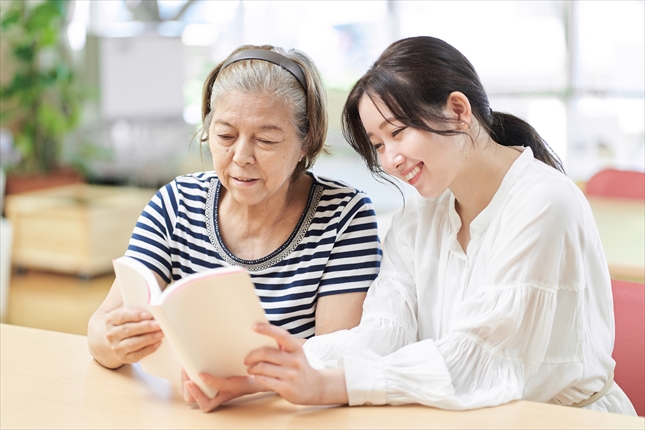 女性家政婦スタッフとご高齢の女性が、共に笑顔で本を読んでいる写真