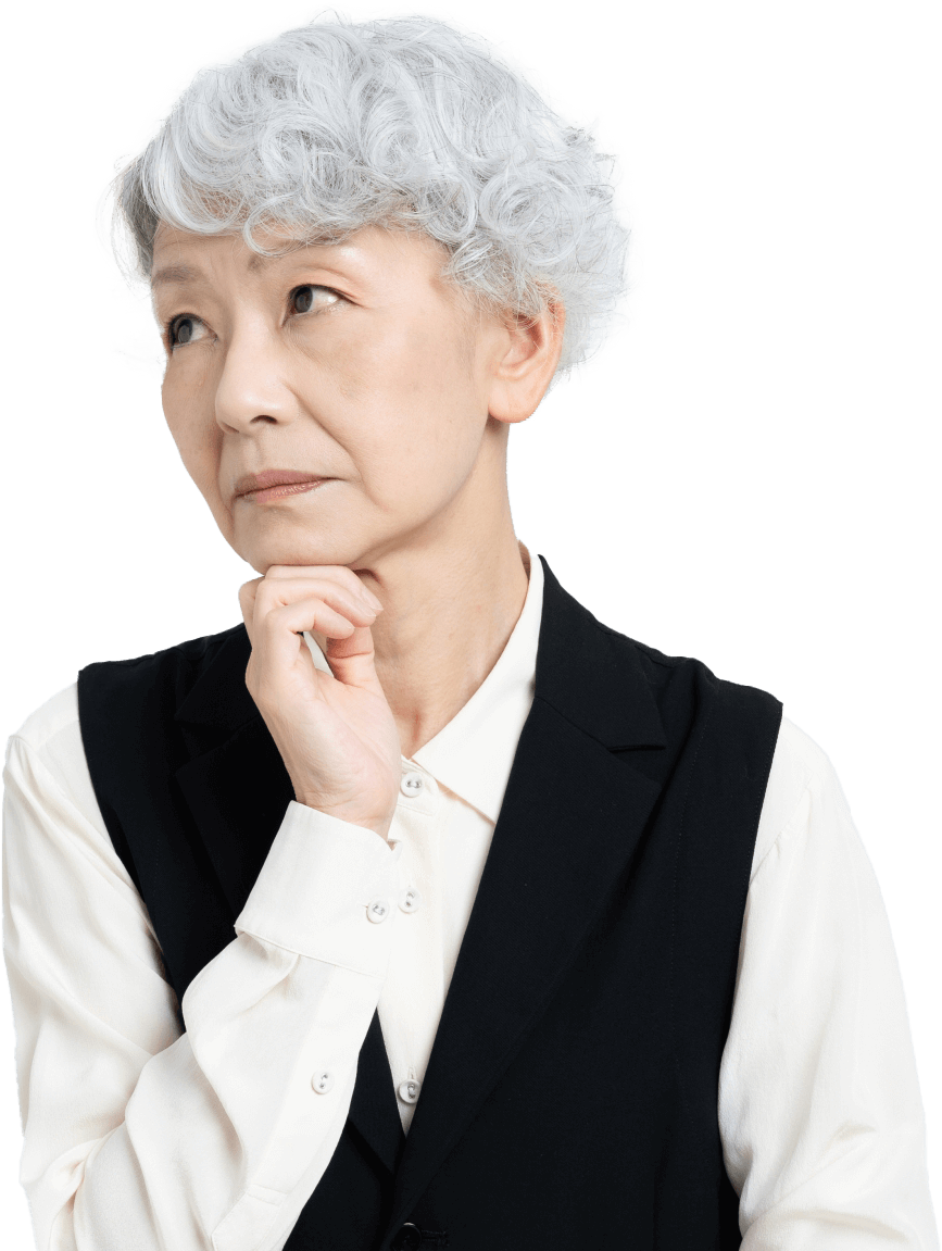白髪のご高齢女性が、困った表情で首を傾げ、片腕を顎につけている写真