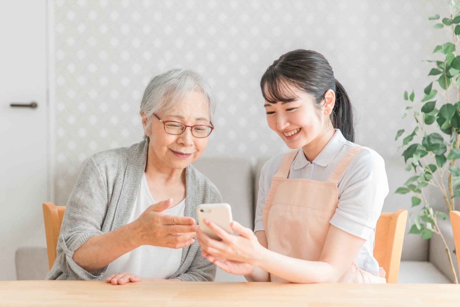 女性家政婦スタッフとご高齢女性が、共にスマートフォンを眺めて笑っている写真
