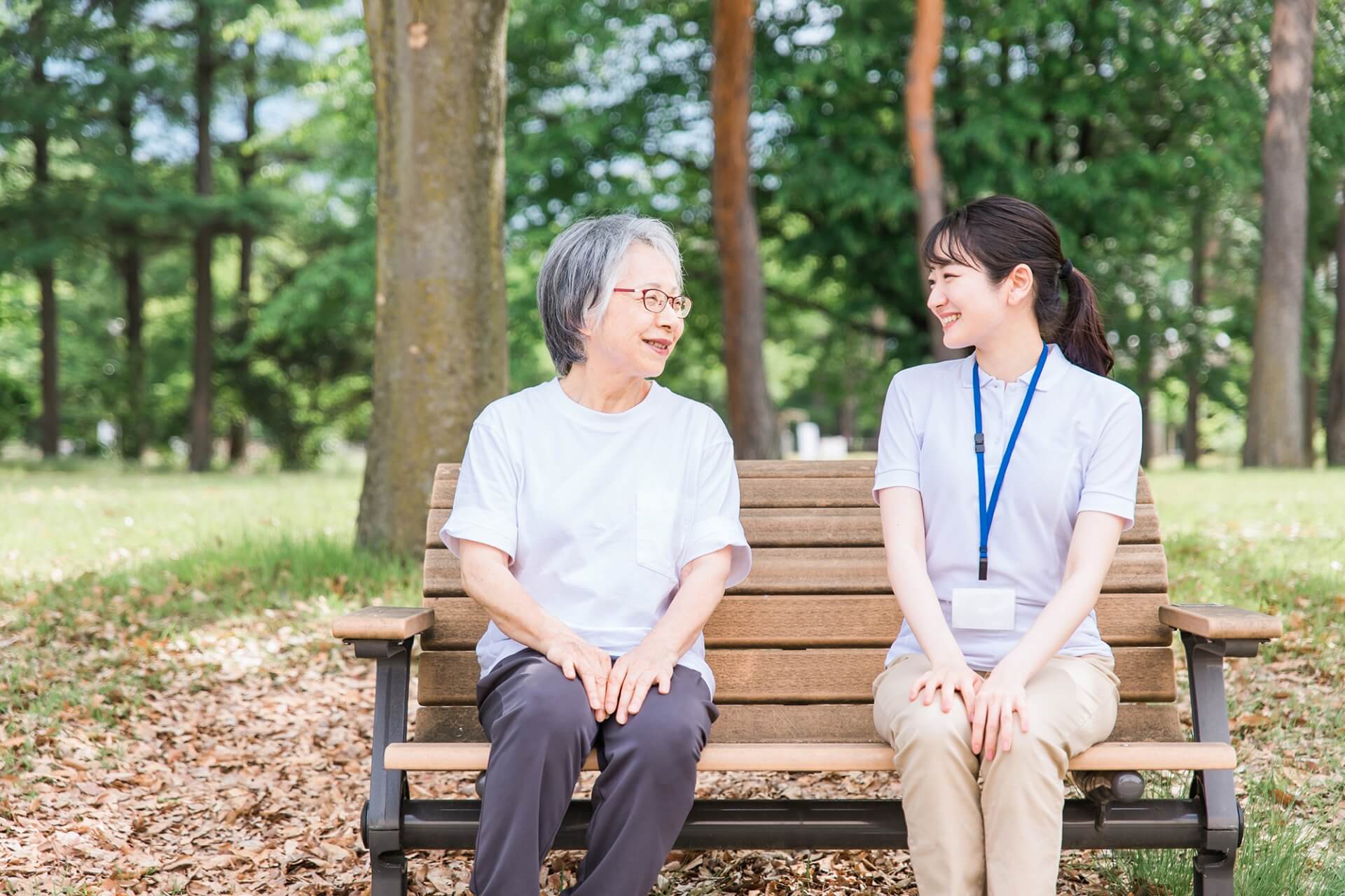 屋外のベンチに座り、親しく会話する高齢女性と介護スタッフの写真