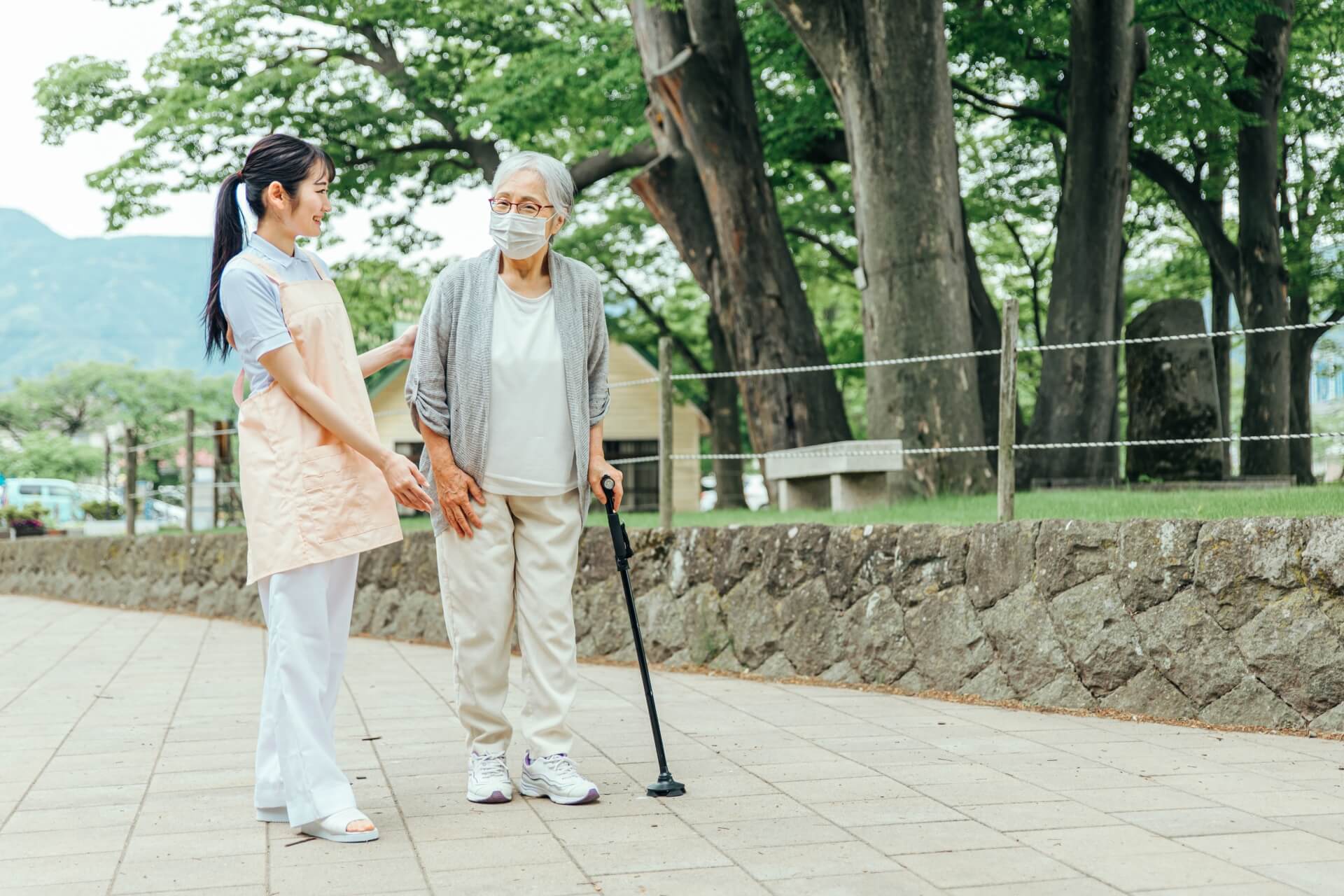 女性介護スタッフと杖をついたご高齢女性が、共に外で散歩を楽しんでいる写真