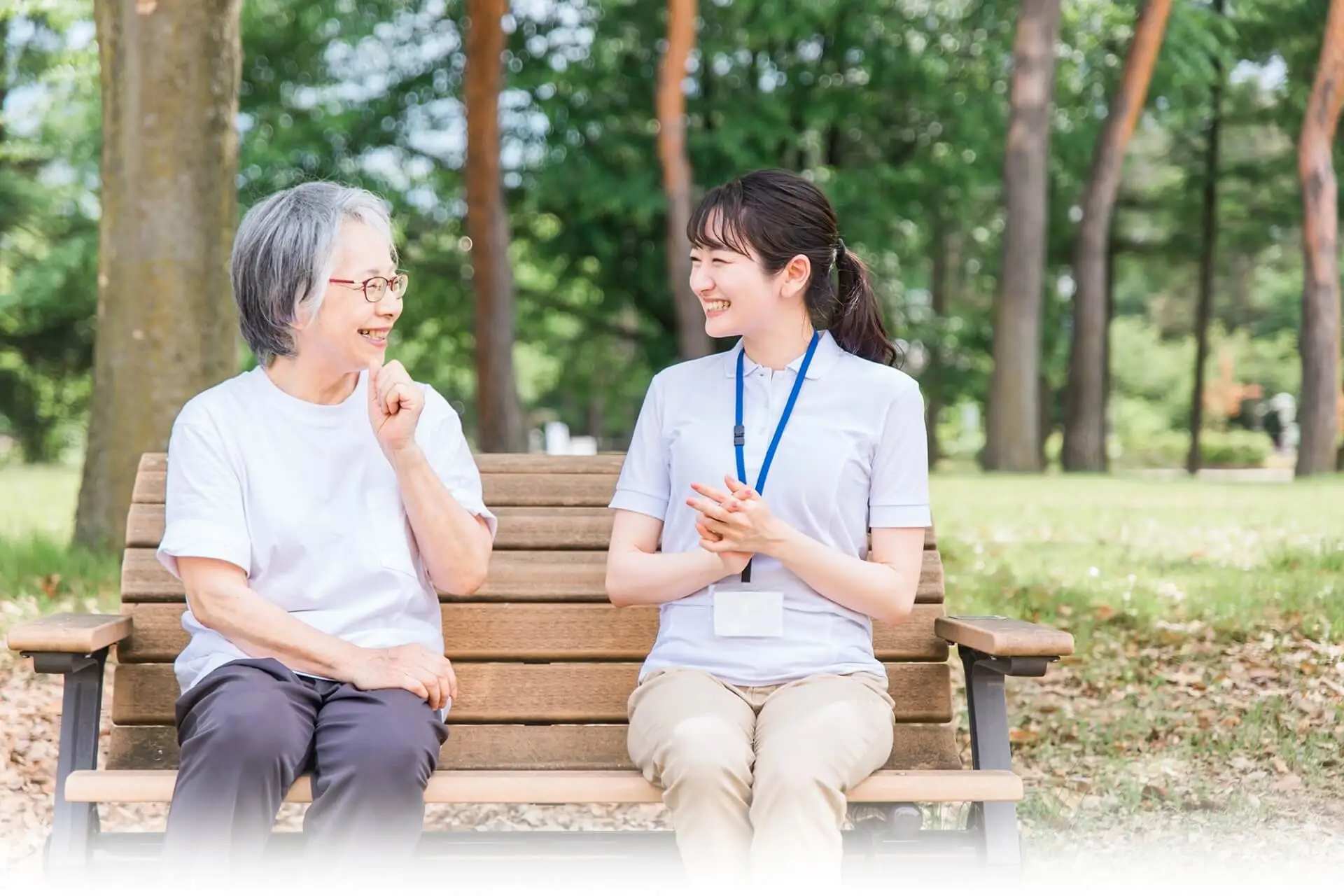 外のベンチに腰掛けて談笑するご高齢女性と女性介護スタッフの写真