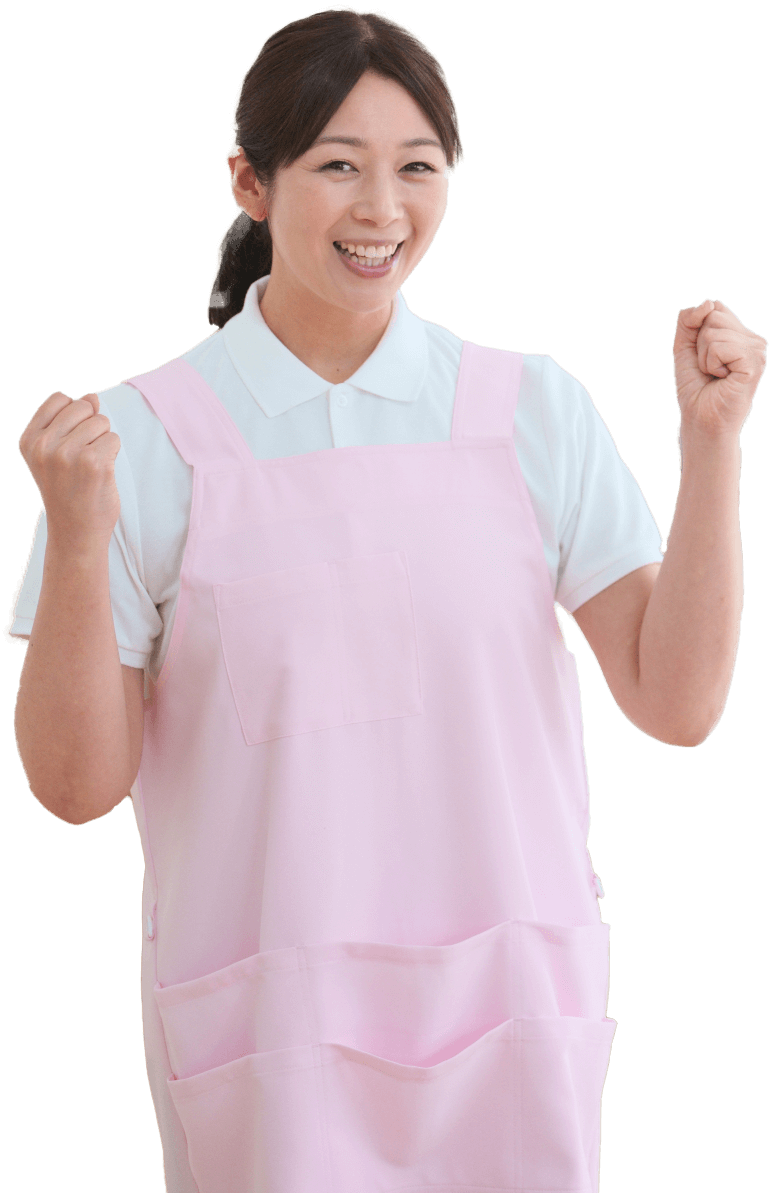 ピンクのエプロンを身につけ、ガッツポーズをしながら笑顔でこちらを見つめる女性介護スタッフの写真