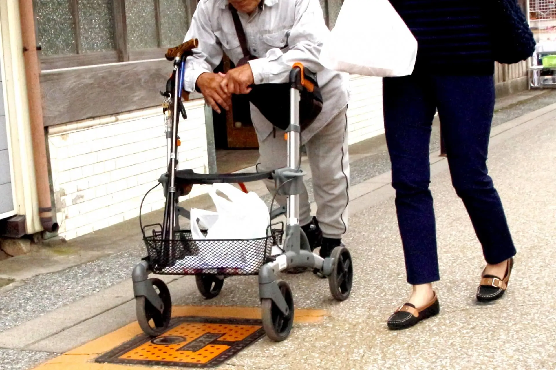 歩行器を使用するご高齢男性と共に、女性スタッフが屋外を歩いている写真