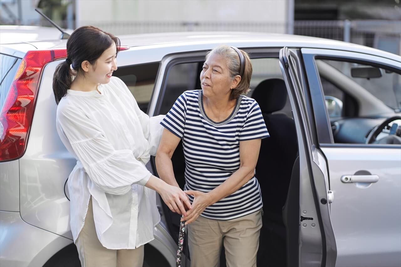 杖をついたご高齢の女性が車から降りるのを介助する女性介護スタッフの写真